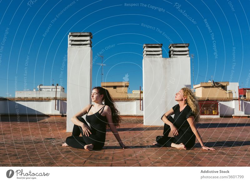 Frauen praktizieren gemeinsam Yoga auf dem Dach Zusammensein Dachterrasse Terrasse üben Pose positionieren ardha matsyendrasana verdrehen Halbherr der Fische