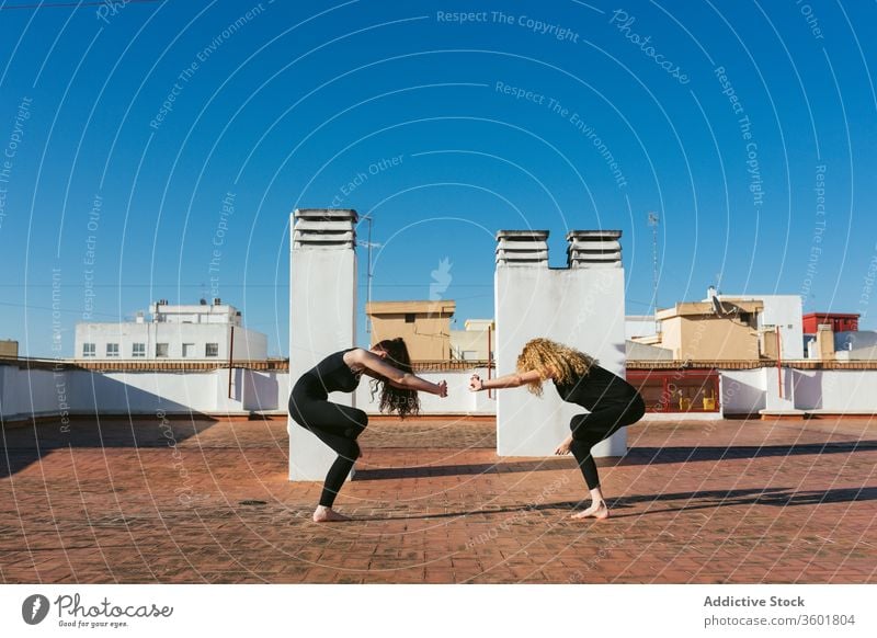 Frauen praktizieren gemeinsam Yoga auf dem Dach Zusammensein Dachterrasse Terrasse üben Pose positionieren verdrehen Akro-Yoga Mutter Tochter Lifestyle Harmonie