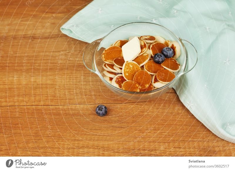 Mini-Pfannkuchen mit Butter und Heidelbeeren liegen in einem Teller auf einem Holztisch. Brunch, Dessert für Kinder, Trending Food. Platz für Text Müsli