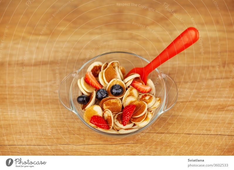 Mini-Pfannkuchen mit Erdbeeren und Blaubeeren in einer Schale auf einem Holztisch, Draufsicht. Trendiges Essen - Pfannkuchen-Cerealien Müsli Lebensmittel