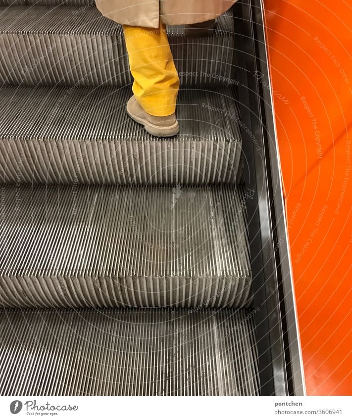 Knallig gelbes Hosenbein trifft knallig orange Seitenwand einer Rolltreppe. Mode und Stil. Unterwegs sein Knallfarben rolltreppe kleidung mode farbkontrast