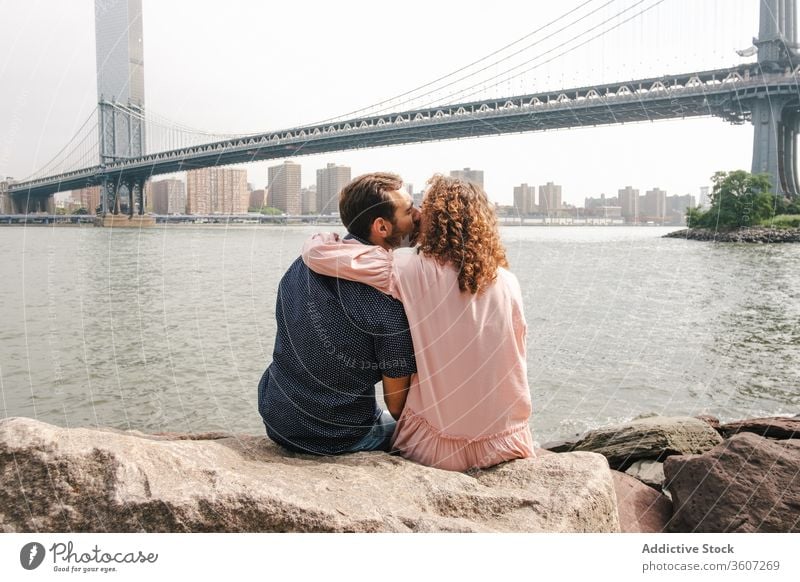 Zärtliches Paar küsst sich am Flussufer in New York Partnerschaft Zusammensein Kuss romantisch Umarmung Brooklyn Bridge Angebot schlendern New York State