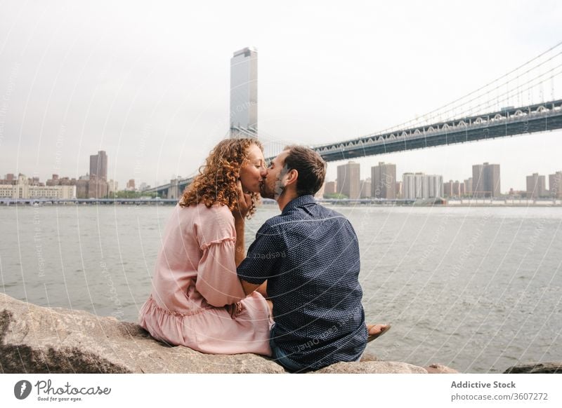 Zärtliches Paar küsst sich am Flussufer in New York Partnerschaft Zusammensein Kuss romantisch Umarmung Brooklyn Bridge Angebot schlendern New York State