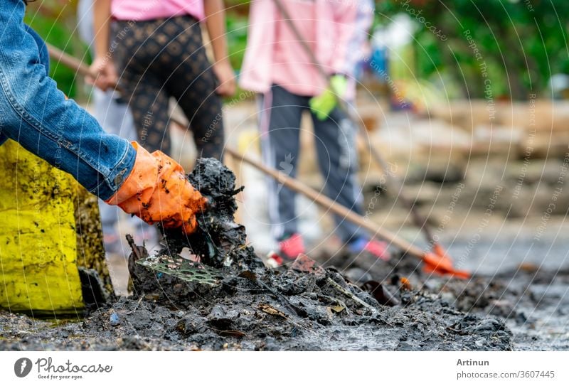 Freiwillige Erwachsene und Kinder, die am Meeresstrand Müll sammeln. Umweltverschmutzung am Strand. Aufräumen von Müll am Strand. Die Menschen tragen orange Handschuhe und sammeln den Müll in einem gelben Sack ein.