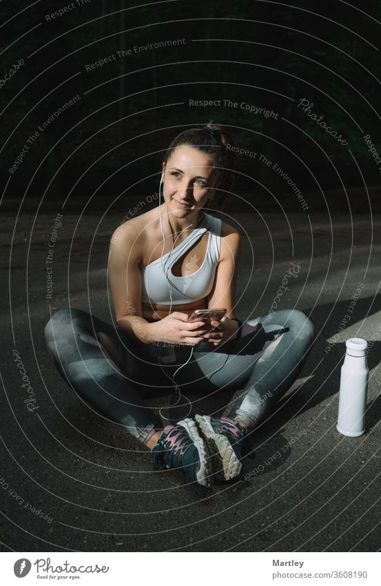 Porträt eines jungen, fitten, hübschen Mädchens, das auf der Straße sitzt und Textnachrichten auf dem Smartphone tippt. Frau, die ihr Telefon nachmittags auf der Straße benutzt.