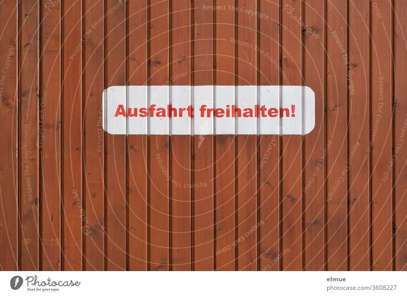 weißer Aufkleber mit roter Druckschrift "Ausfahrt freihalten!" an einer braunen Holzwand Parkverbot Schrift Buchstabe privat Einfahrt Tor Aufforderung