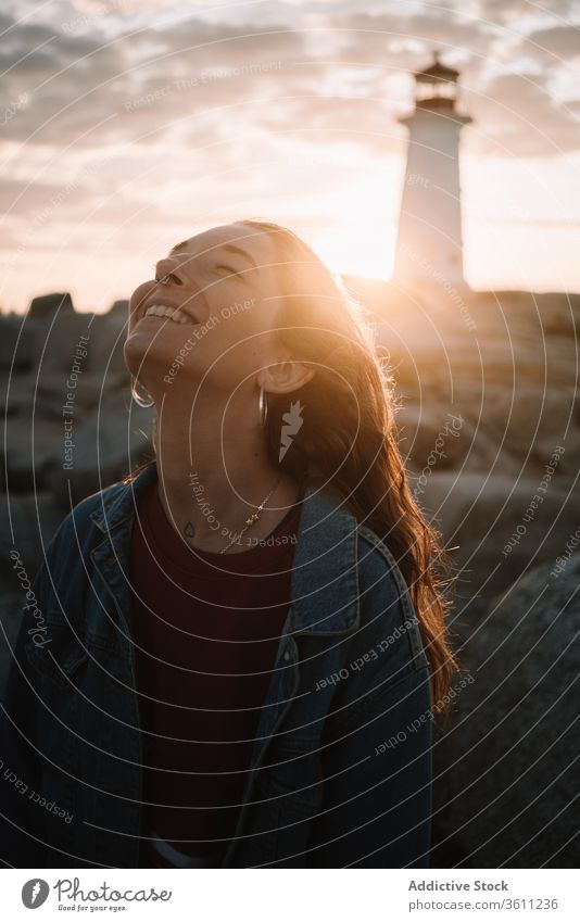 Glückliche Frau gegen Sonnenuntergangshimmel und Leuchtturm reisen Lachen Himmel wolkig Peggys-Bucht Kanada jung Abend Abenddämmerung Dämmerung Lächeln lässig