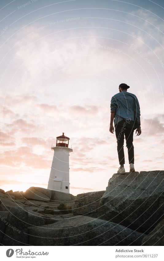 Unbekannter Mann auf Stein in der Nähe des Leuchtturms bewundern Sonnenuntergang Himmel wolkig Tourist Peggys-Bucht Kanada männlich Abend Felsen Abenddämmerung