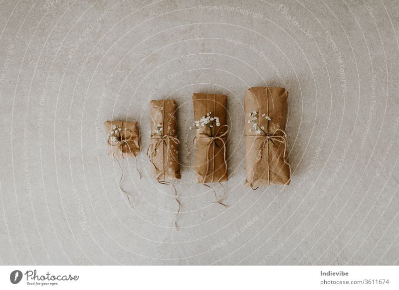 Vier in Papier verpackte Geschenke mit Trockenblume und Schnur auf Marmorgrund. Null-Abfall-Verpackungsidee für Weihnachten, Geburtstag. Wiederverwendbare Verpackung mit Hanfschnur.