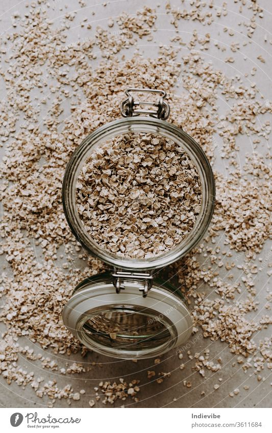 Organische Haferflocken und ein Glas mit Glas auf grauem Hintergrund. Gesunde Frühstückszutat für Porridge. Voller Vitamine, Mineralien und Ballaststoffe.