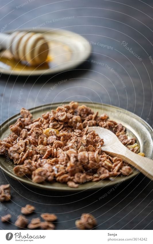 Granola auf einem goldenen Teller mit einem Holzlöffel, rustikaler Hintergrund Müsli Schokolade Nuss Dessert Frühstück Lebensmittel Ernährung Getreide frisch