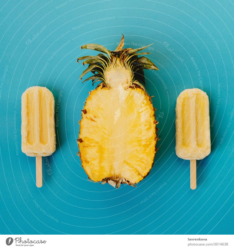 Tropischer Flachschlag aus drei veganen Eis am Stiel und der Hälfte einer reifen Ananas auf cyanfarbenem Hintergrund saisonbedingt Sommer kalt Dessert