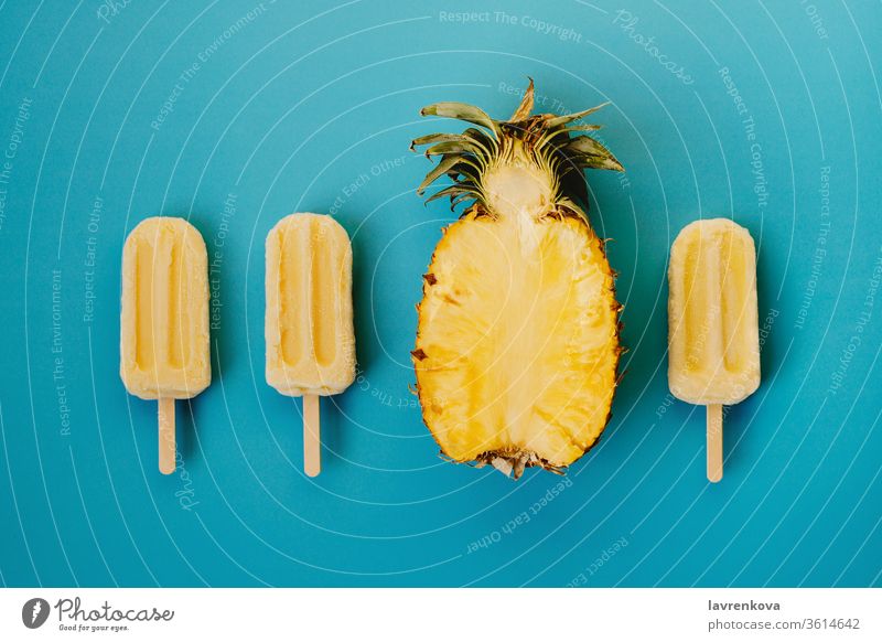 Tropischer Flachschlag aus drei veganen Eis am Stiel und der Hälfte einer reifen Ananas auf cyanfarbenem Hintergrund saisonbedingt Sommer kalt Dessert