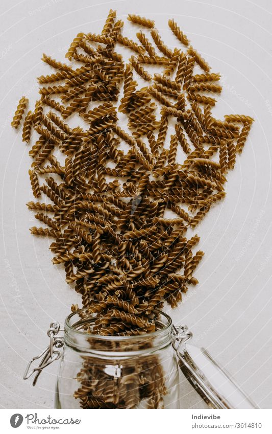 Ein Haufen grüner ungekochter Bio-Fusilli-Nudeln auf grauem Hintergrund mit Glasbehälter Spätzle fussili Italienisch roh Spinat trocknen lang Regal Leben