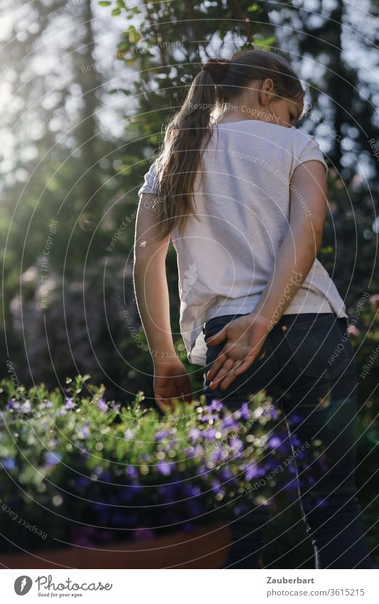 Mädchen mit Pferdeschwanz im Gegenlicht, in Bewegung, hinter lila Blumen Kind Hände Arme T-Shirt weiß schön hübsch süß Garten schauen Kindheit Sommer sommerlich