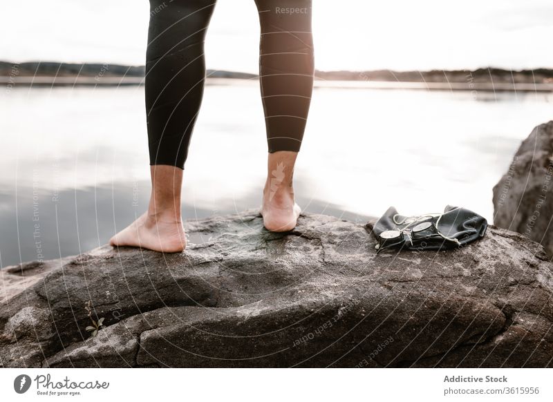 Gesichtsloser Sportler, der vor dem Tauchen barfuss auf einem Felsen steht Taucher Neoprenanzug See Schutzbrille Wasser Abend Felsbrocken Inspiration