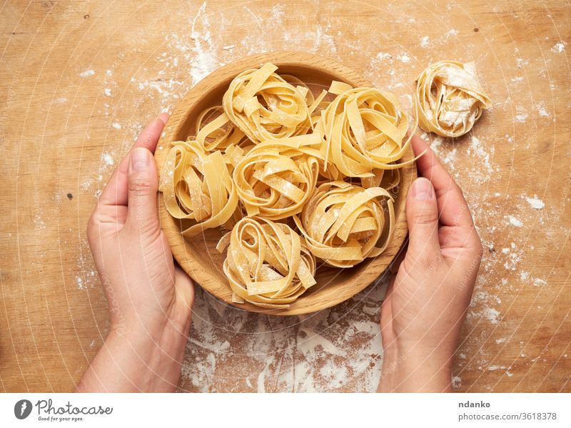 Frauenhände, die einen Holzteller mit rohen Fettuccine-Nudeln halten orange Spätzle gerollt Hand Halt Teller trocknen Mehl Lebensmittel frisch Haufen