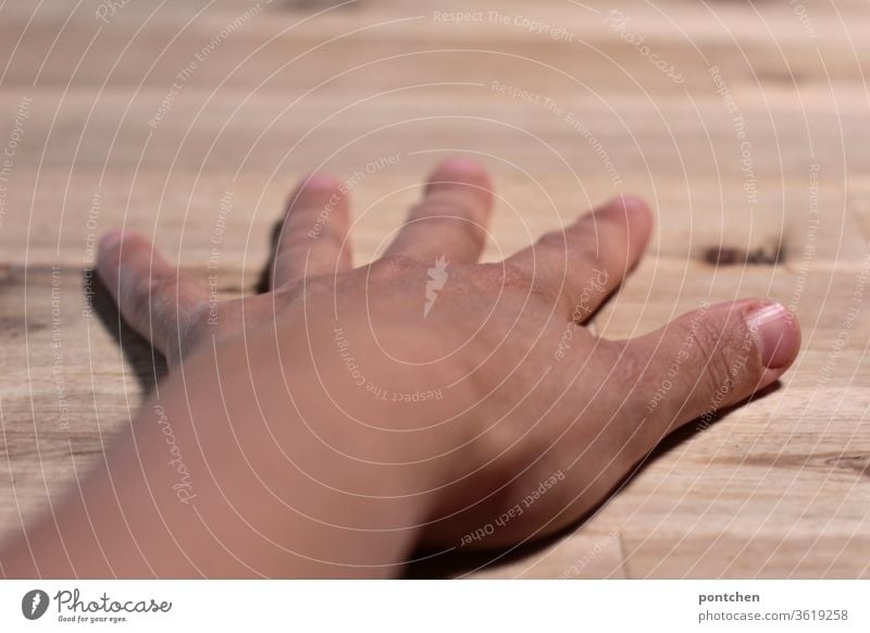 Eine linke,  weibliche, braungebrannte Hand  mit gespreizten  Fingern liegt auf einer Tischplatte  aus Holz.  Dominanz hautfarbe finger tischplatte fingernägel