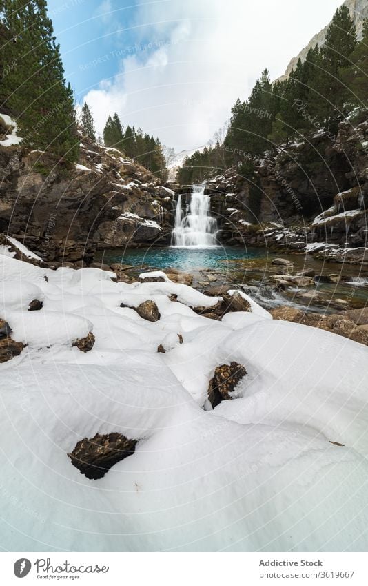 Wasserfall mit Pool zwischen schneebedeckten Bergen Berge u. Gebirge Schnee Wald Natur Landschaft Winter wild strömen malerisch Umwelt Felsen Harmonie kalt