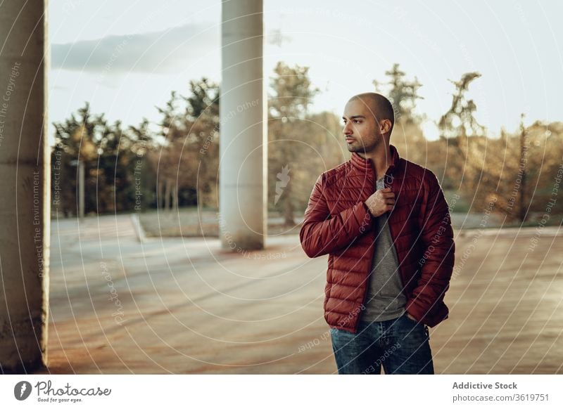 Junger Mann in modischem Outfit steht auf der Straße jung modern selbstbewusst Jacke warme Kleidung besinnlich Hipster unrasiert Herbst Vollbart nachdenklich