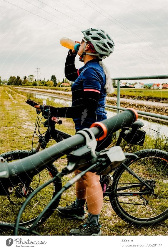 Junge Frau trinkt beim Mountainbiken aus einer Fahrradflasche Sport sportlich Athlet Spaß Schutzhelm Trikot Außenaufnahme Fitness Fahrradfahren Gesundheit