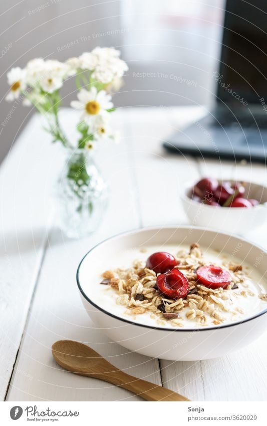 Müsli mit Joghurt und Kirschen auf einem weißen Holztisch und ein Laptop. Gesundes Frühstück. Haferflocken Schalen & Schüsseln laptop Holztür Homeoffice