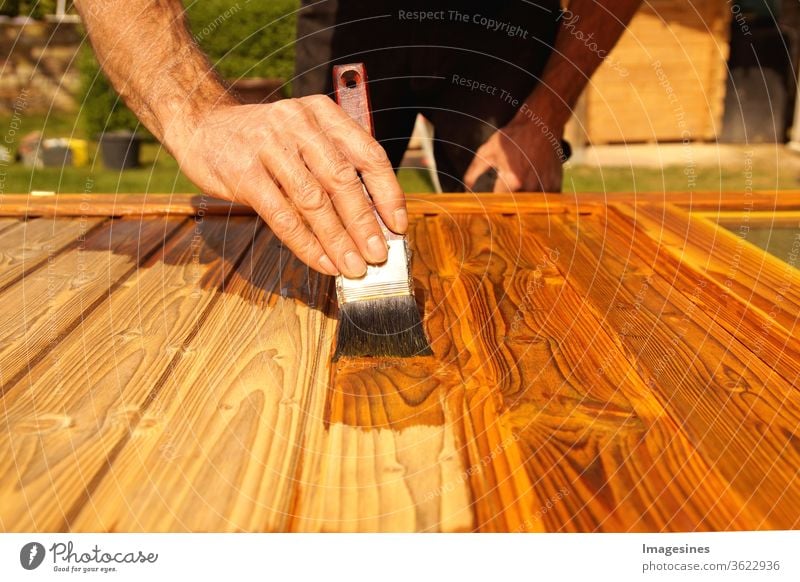 Lasieren. Holzarbeiten, streichen von Holz. Hand des Handwerkers, der eine Holztür lackiert. Konzept der Renovierungsarbeiten, Zimmerei  und Holzarbeiten. Maler, der Holzoberfläche malt, Holzschutz