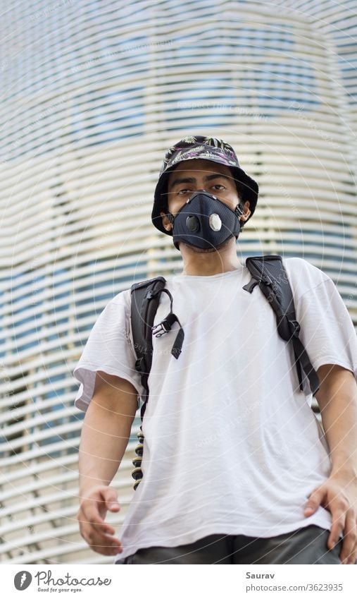 Ein junger Mann im Freien mit einer schützenden Gesichtsmaske zum Schutz vor einer Infektion mit dem Coronavirus, der während einer globalen Pandemie eine mit Blumen bedruckte Eimerkappe und einen Beutelpack trägt.