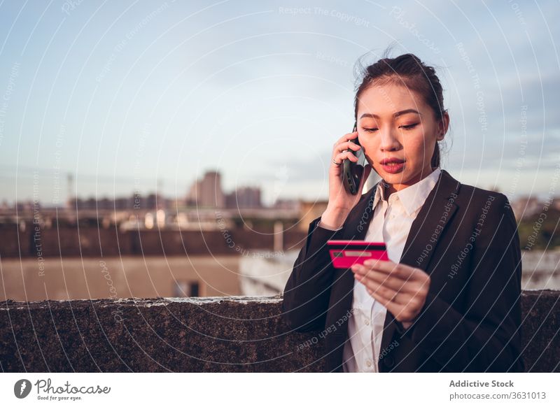 Vielbeschäftigte ethnische Frau mit Kreditkarte telefoniert Telefonanruf ernst reden Smartphone Problematik diskutieren formal jung asiatisch Geschäftsfrau