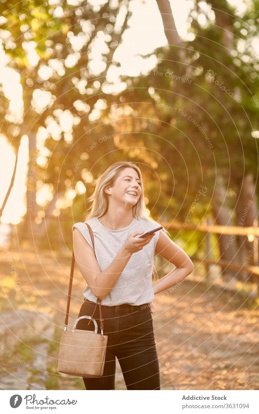 Glückliche Frau mit Smartphone im Park stehend heiter benutzend genießen Browsen jung trendy Lifestyle Apparatur Gerät ruhen Kälte positiv soziale Netzwerke