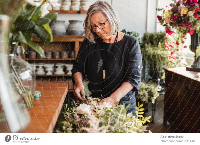 Reife Frau arrangiert Blumen im Geschäft Floristik Blumenstrauß grün Pflanze kreieren wählen komponieren einrichten Designer dekorativ kreativ Arbeit Beruf