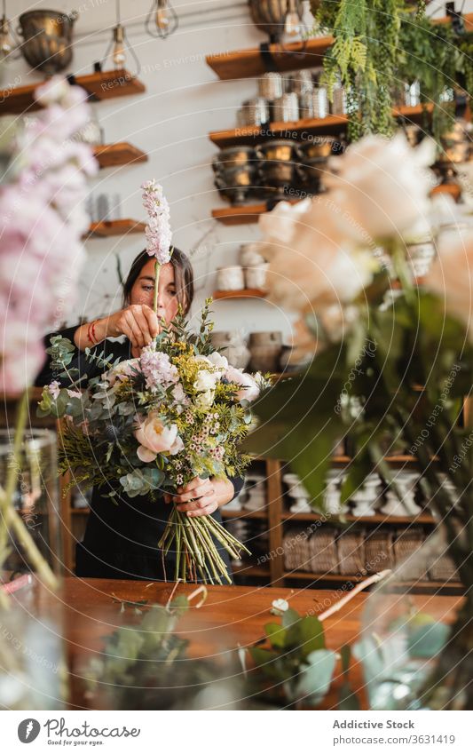 Florist mit Blumenstrauss arbeitet im Geschäft Floristik Frau Blumenstrauß einrichten kreieren konzentriert Blütezeit heiter komponieren Designer dekorativ