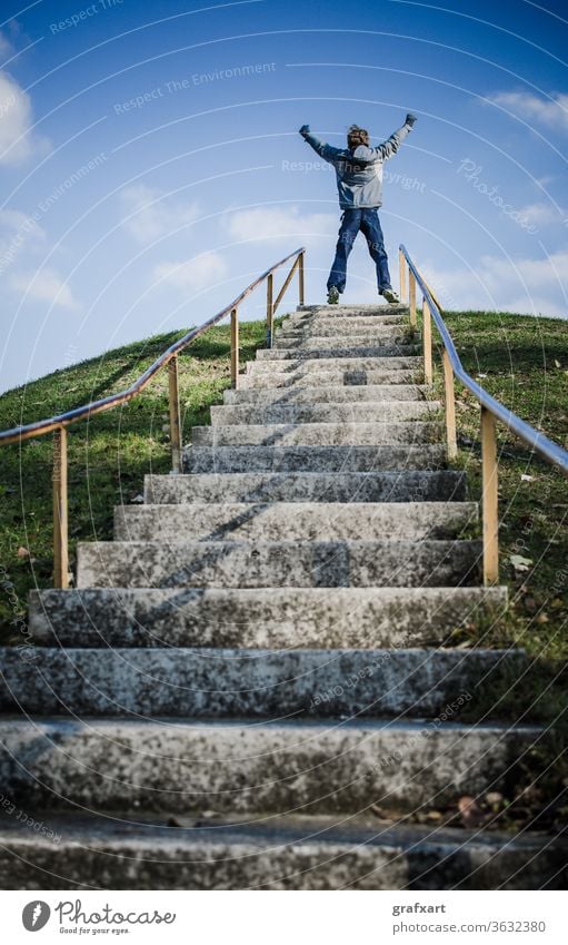 Junge in Siegespose am Ende einer Stiege im Freien leistung ambitioniert business karriere feiern herausforderung champion kind klima konzept entfernung