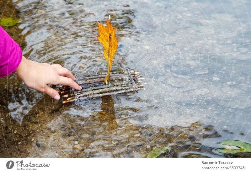 Teenager-Mädchen, das am Spätherbsttag ein handgefertigtes kleines Spielzeugfloß aus Holz in den Bach stellt. Nahaufnahme von Hand hölzern Floß Segel Wasser