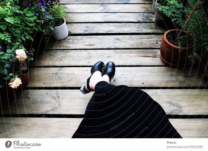 Abends zwischen Blumen auf der Dachterrasse streckt die ältere Frau gern ihre Beine weit von sich. Kleid Schuhe Blumentopf Rosen Glockenblume Wiesenraute