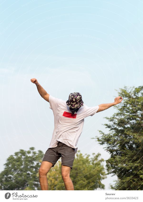 Ein junger Erwachsener, der eine Schutzmaske trägt, um eine Infektion mit dem Coronavirus zu vermeiden, während er einen Ollie-Stunt auf seinem Skateboard im Freien auf einer leeren Straße macht.