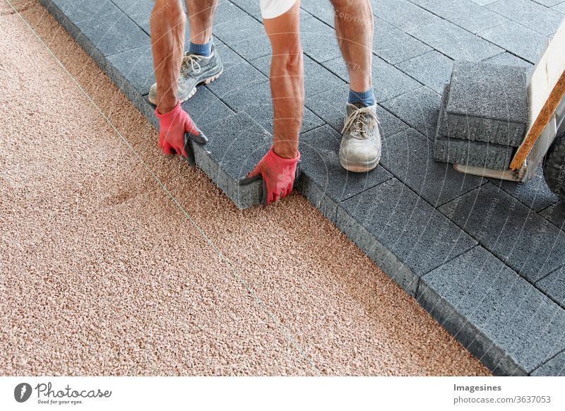 Pflastersteine legen. Pflastern auf Spilt mit einer Schnur, an der Kante platzieren. Hände eines Arbeiters, der Pflasterstein, große Betonpflastersteine ​​legt. Verlegen von Betonplatten. Bauherr, der Pflastersteine ​​in Basaltsplitt setzt