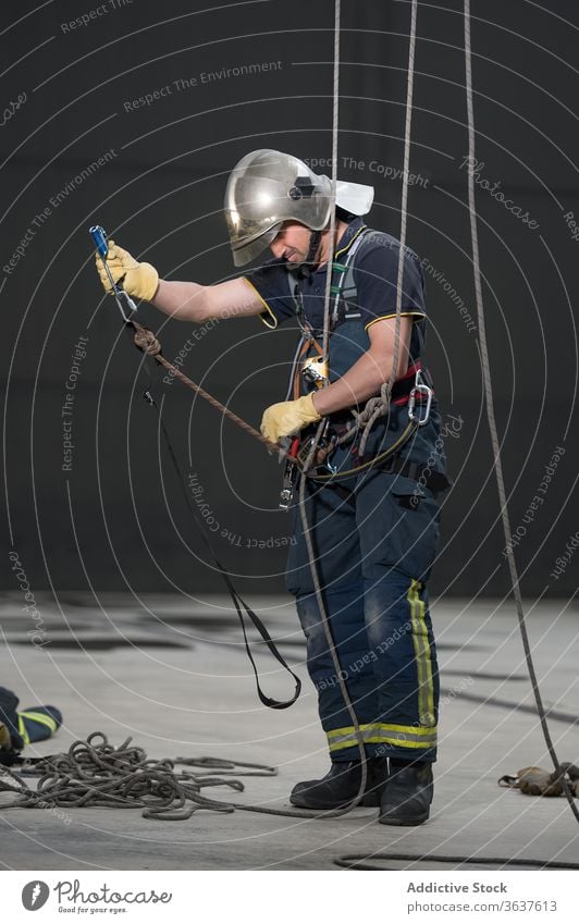 Männlicher Feuerwehrmann mit Seilen im Trainingskomplex Gerät üben Uniform behüten ausrichten männlich Mut stark retten Schutzhelm physisch aktiv professionell