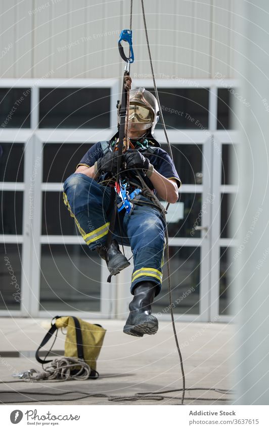 Männlicher Feuerwehrmann mit Seilen im Trainingskomplex Aufstieg Gerät Mut stark Gebäude üben männlich retten Uniform behüten Schutzhelm physisch aktiv