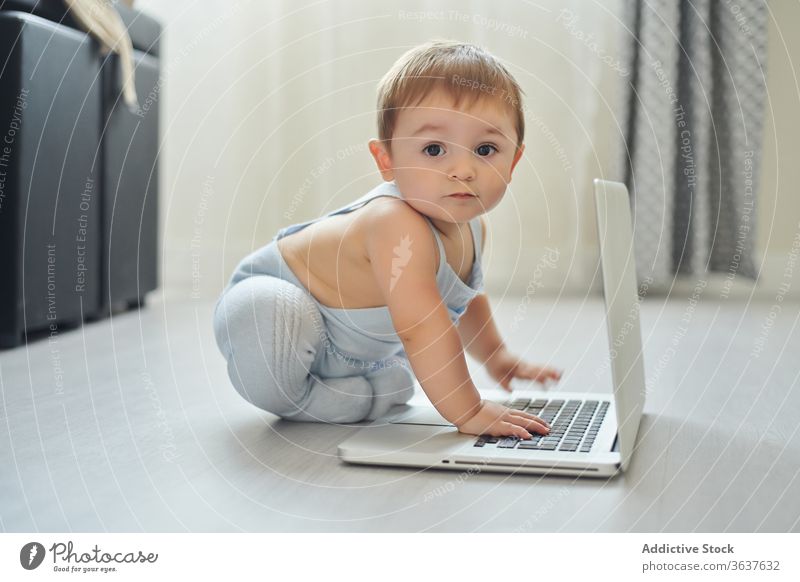 Fröhliches Baby spielt zu Hause mit dem Laptop Glück benutzend heimwärts spielen Kleinkind Apparatur modern Kindheit Lifestyle wenig allein heiter Gerät Netbook