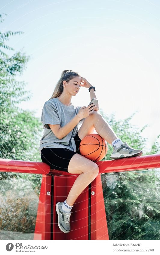 Sportlerin mit Basketball-Ball und Smartphone auf dem Spielplatz Frau benutzend Gericht ernst jung ruhen Browsen Telefon Mobile Athlet Training Aktivität