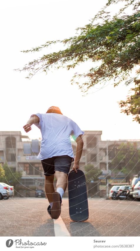 Ein junger Erwachsener stürmt bei Sonnenaufgang mit seinem Skateboard auf einer leeren Straße vor. Sommer Skateboarding Erholung covid-19 leere Straße