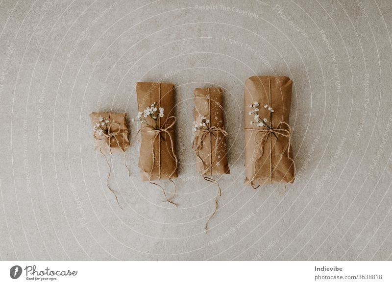 Vier in Papier verpackte Geschenke mit getrockneten Blumen und Schnur auf Marmorgrund Paket Verpackung Feiertag Überraschung wiederverwendbar