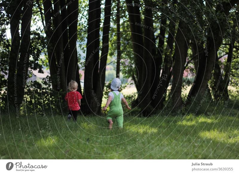 zwei kleine klinder rennen auf einer wiese zu einem Bach Bäume Wiese Lichtung fangen fangen spielen Latzhose Mütze Kinderspiel Kindheit Sommer grün frei