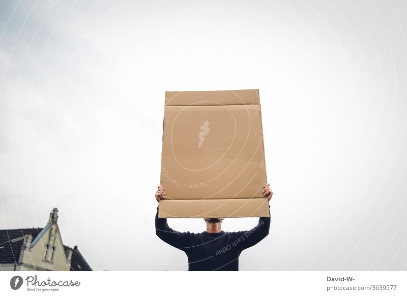 ein Mann hält ein Schild aus Pappe in die Luft und verdeckt sein Gesicht Meinungsäußerung Meinungsfreiheit aufmerksam 1 Mensch neutraler hintergrund Karton