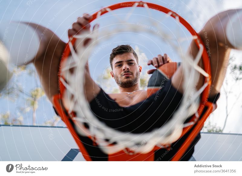 Basketballspieler sitzt auf einem Korb auf dem Spielplatz Reifen Mann Sportler Spieler Training Ball Gesundheit männlich gutaussehend professionell Aktivität