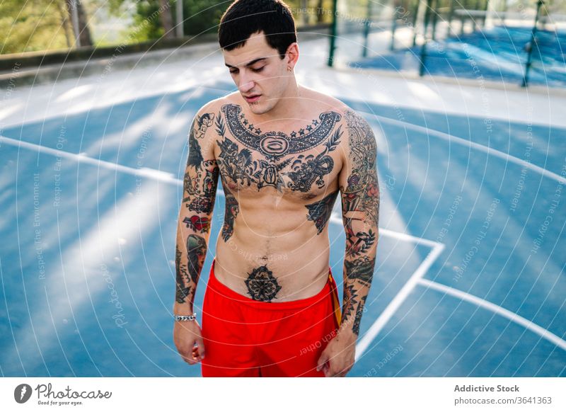 Selbstbewusster männlicher Athlet auf dem Sportplatz Sportler Spielplatz Training ohne Hemd Mann selbstbewusst Tattoo nackter Torso Sportpark Sommer stark