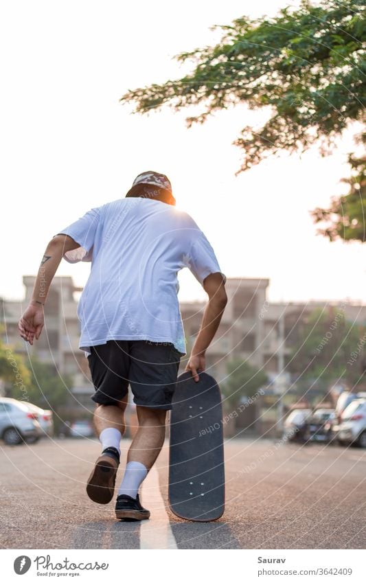 Ein junger Erwachsener stürmt bei Sonnenaufgang mit seinem Skateboard auf einer leeren Straße vor. Sommer Skateboarding Erholung covid-19 leere Straße