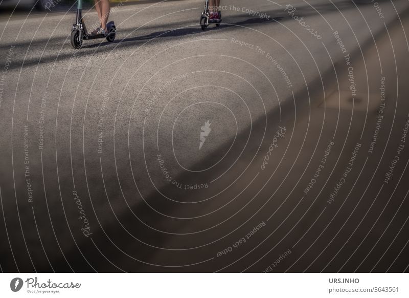 es sind nur die Beine von zwei Frauen, die auf dem heißen Asphalt der Straße mit dem  Cityroller unterwegs sind, zu sehen | Detailansicht mit viel Textfreiraum