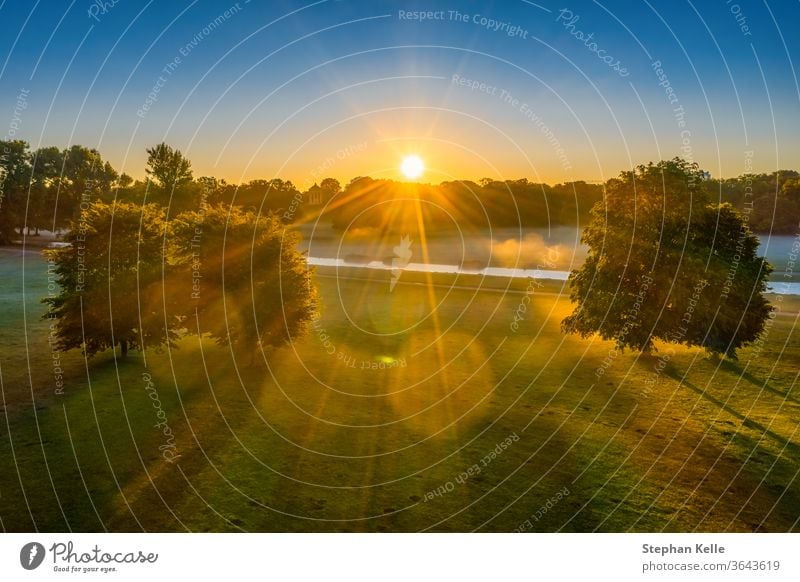 Sonniger Morgen im Park, Luftaufnahmen im Englischen Garten von München, Sonnenstrahlen scheinen durch eine Baumgruppe Natur neblig Wiese grün Sitzung Punkt